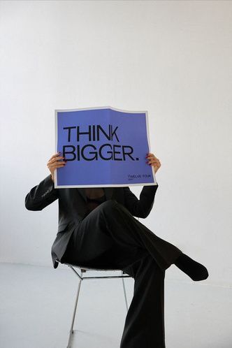 Image of someone sitting down holding a big piece of paper having the words written "Think Bigger"
